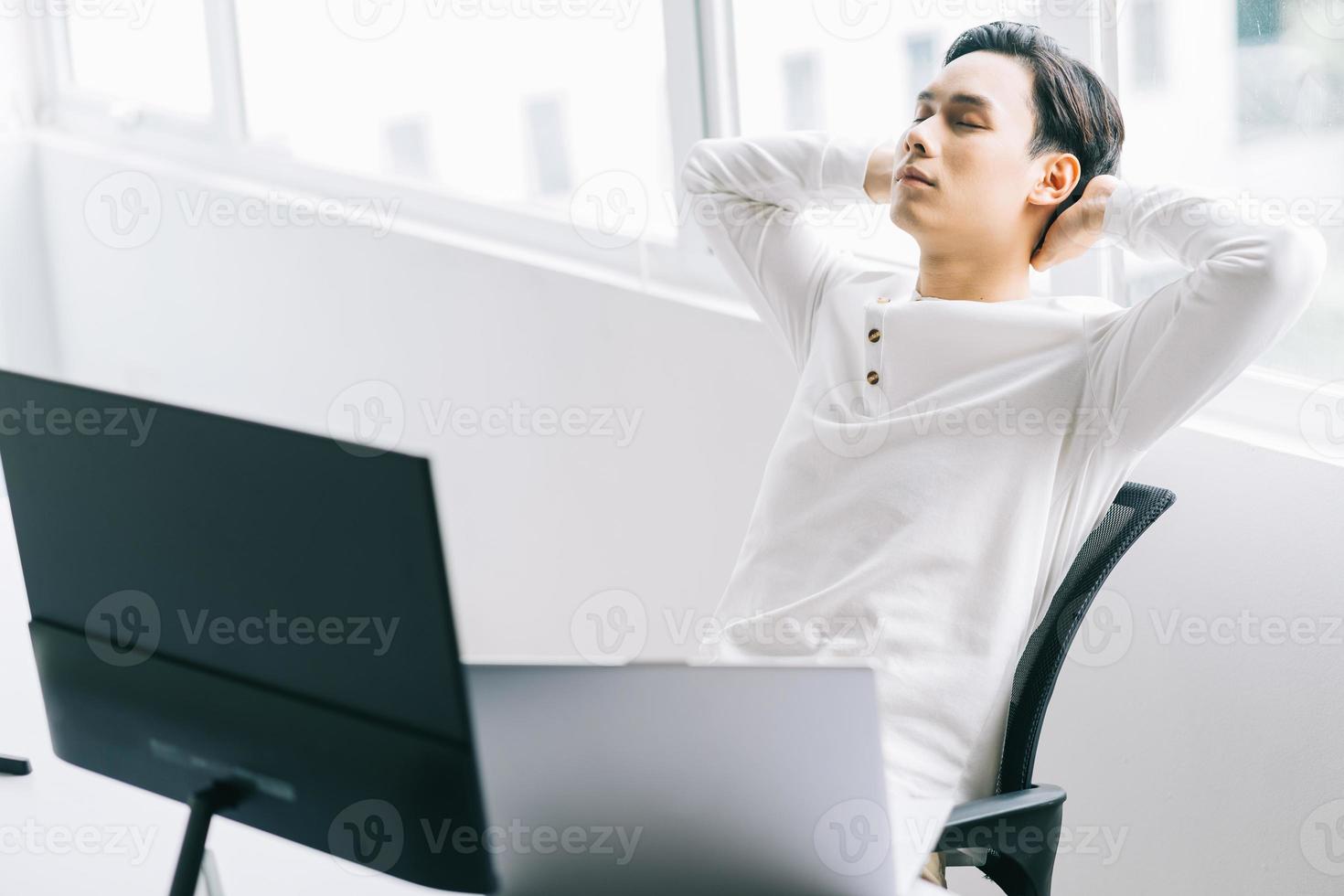 Programador asiático se sienta con la cabeza hacia atrás en su silla para relajarse después de un agotador tiempo de trabajo foto