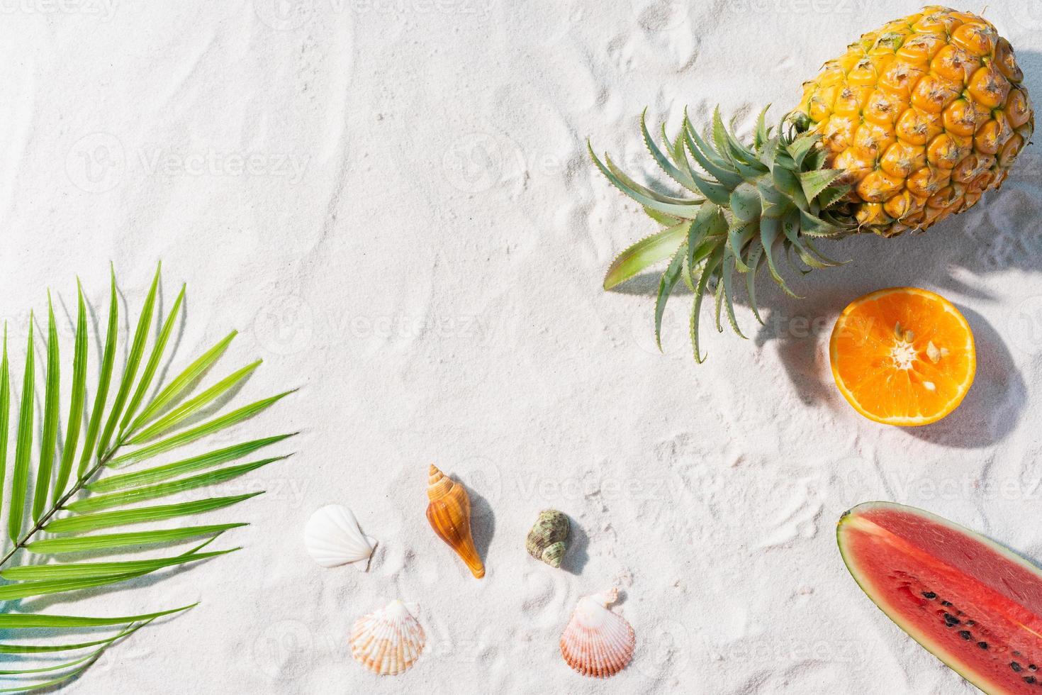 The sandy beach is decorated with tropical fruits and palm leaves photo