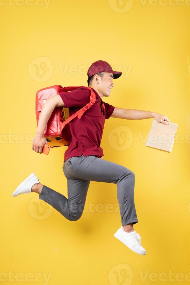 Repartidor asiático vistiendo un uniforme rojo posando sobre fondo amarillo foto