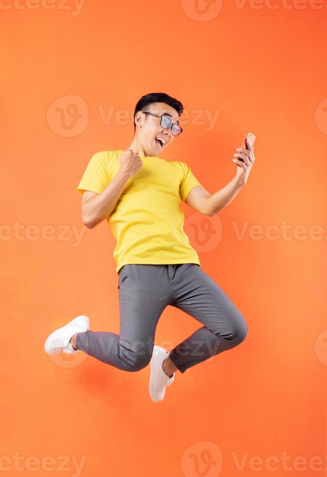 Hombre asiático en camiseta amarilla saltando sobre fondo naranja foto