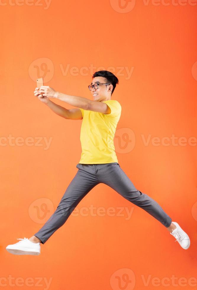 Hombre asiático en camiseta amarilla saltando sobre fondo naranja foto