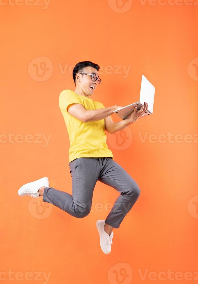Hombre asiático en camiseta amarilla saltando sobre fondo naranja foto