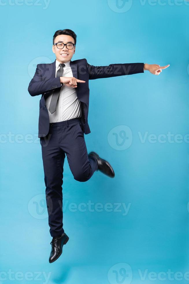 Buisnessman asiático vistiendo traje y saltar sobre fondo azul. foto