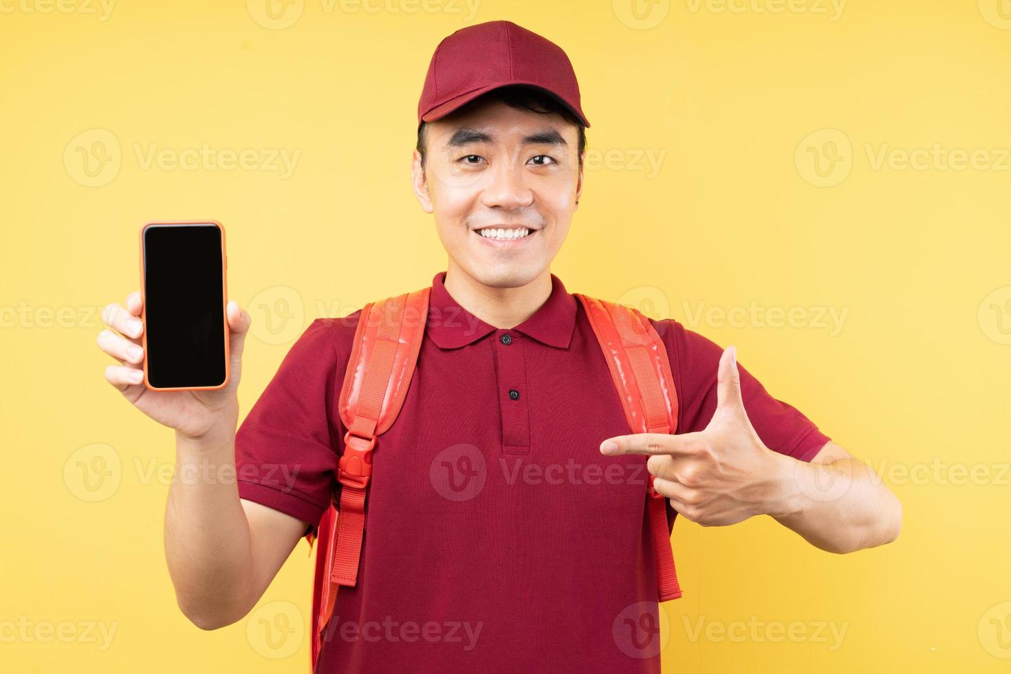 Repartidor asiático vistiendo un uniforme rojo posando sobre fondo amarillo foto