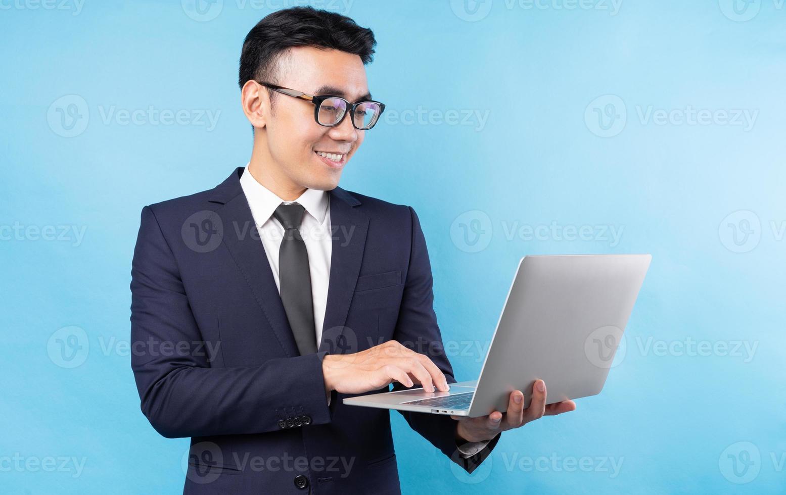 Buisnessman asiático vistiendo traje y usando la computadora portátil sobre fondo azul. foto