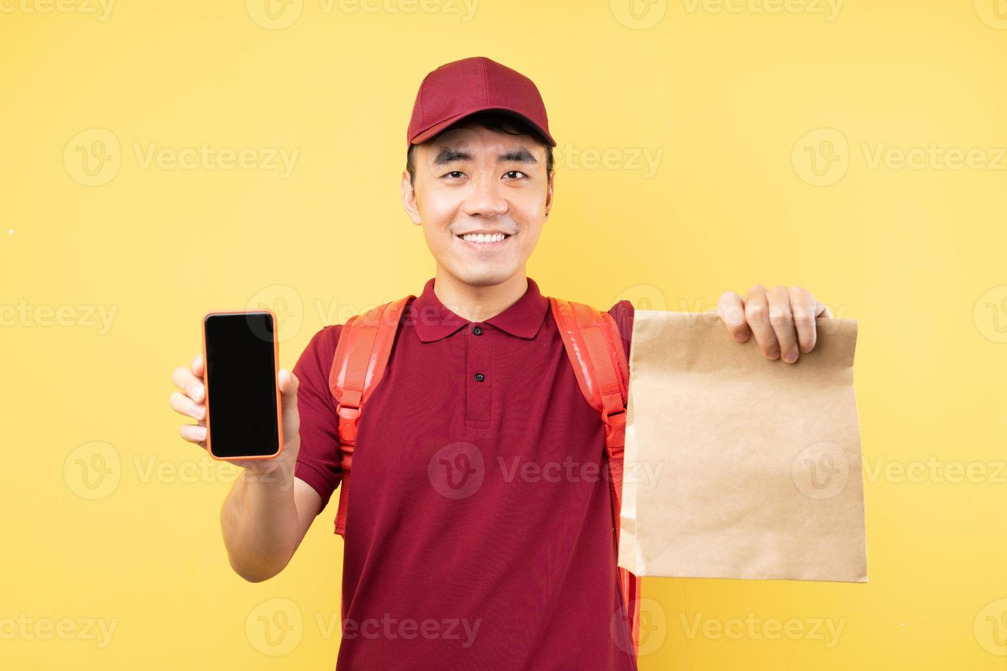 Asian delivery man wearing a red uniform posing on yellow background photo