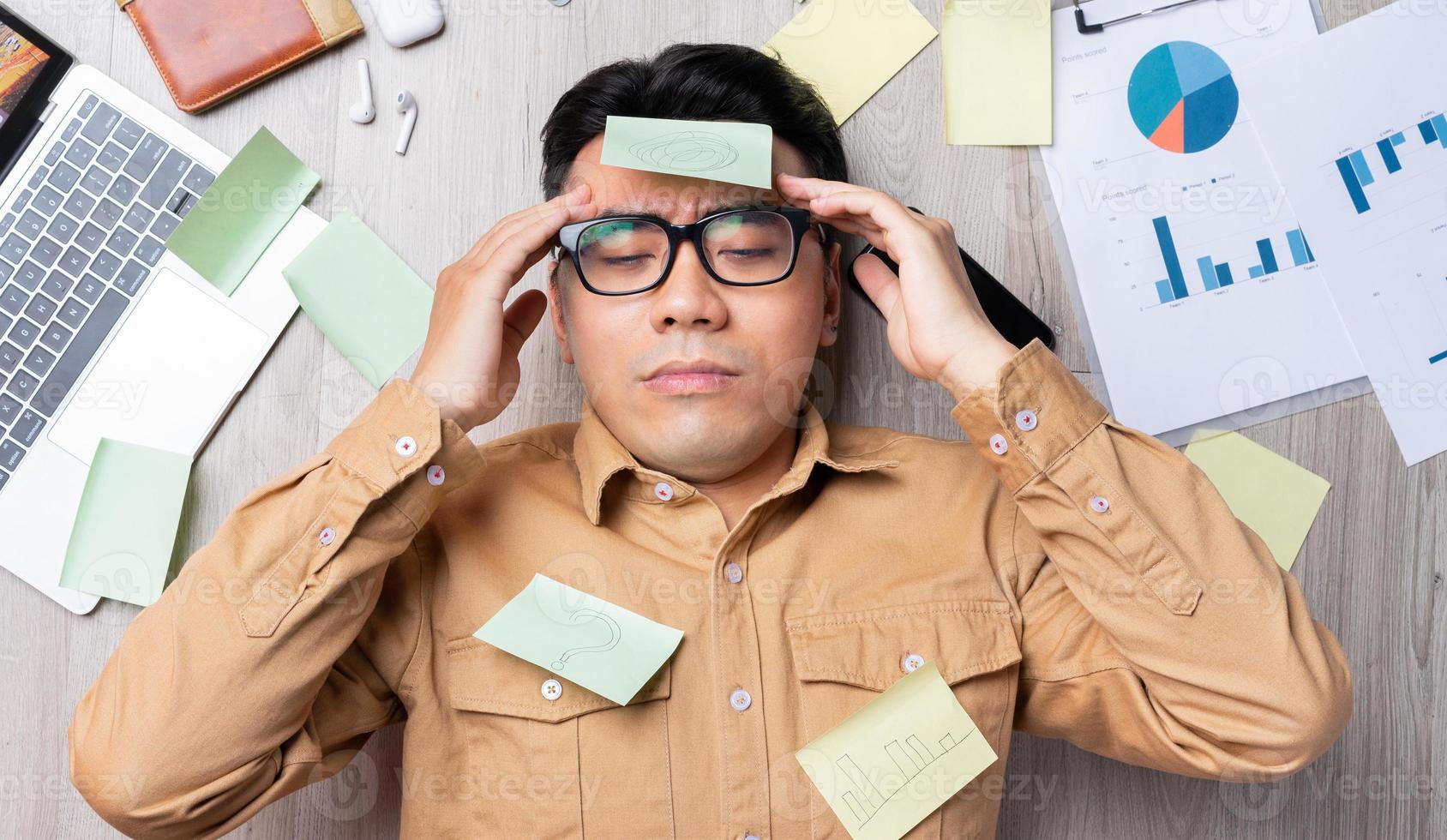 Asian man lying on pile of papers and feeling tired from work photo