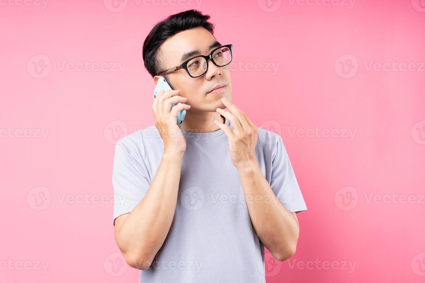 Retrato de hombre asiático con smartphone sobre fondo rosa foto