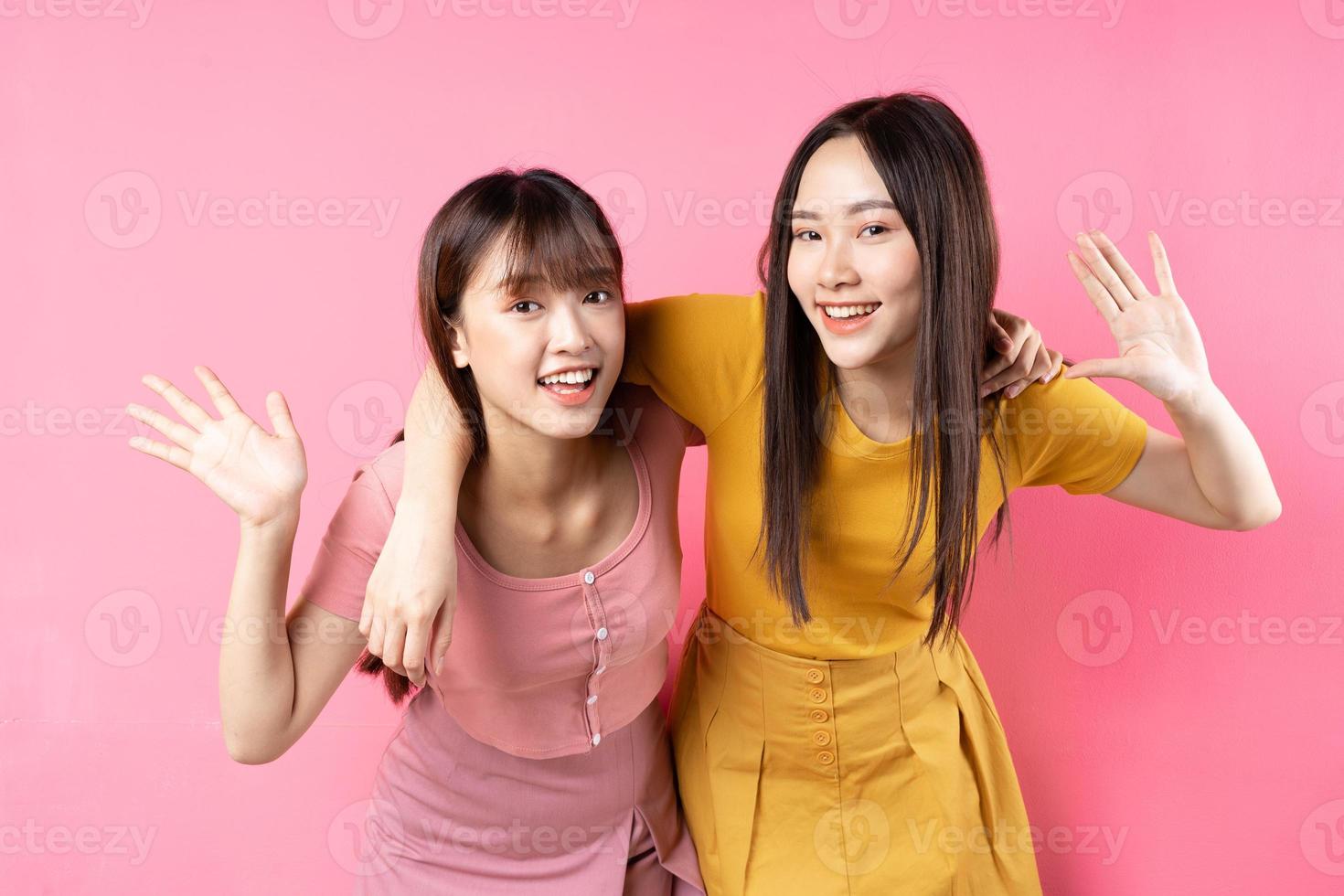 Portrait of two beautiful young Asian girls posing on pink background photo