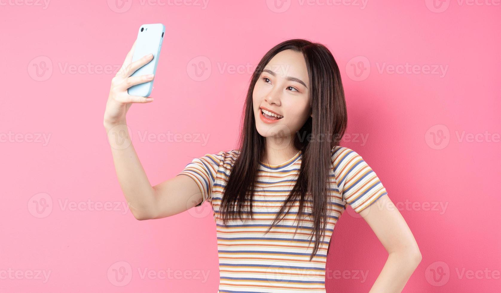 Joven mujer asiática con smartphone sobre fondo rosa foto