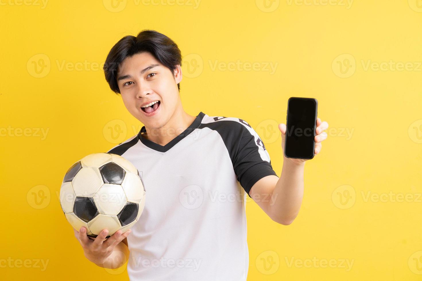 el hombre asiático está sosteniendo una pelota y apuntando al teléfono con una pantalla en blanco foto