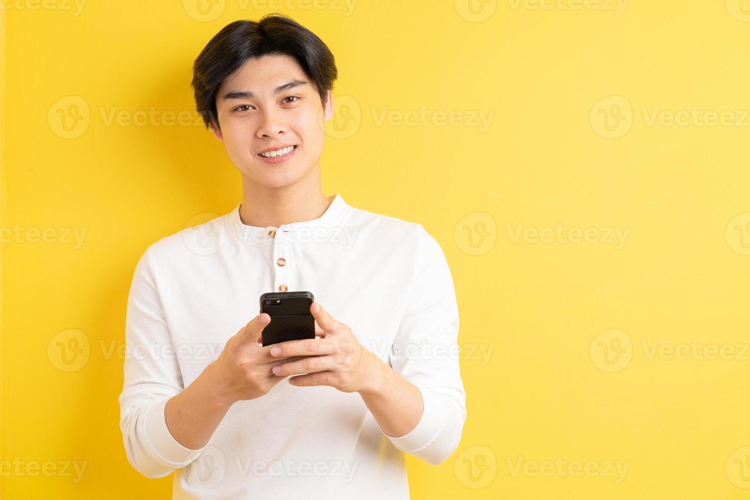 Hombre asiático usando su teléfono para enviar mensajes de texto sobre un fondo amarillo foto