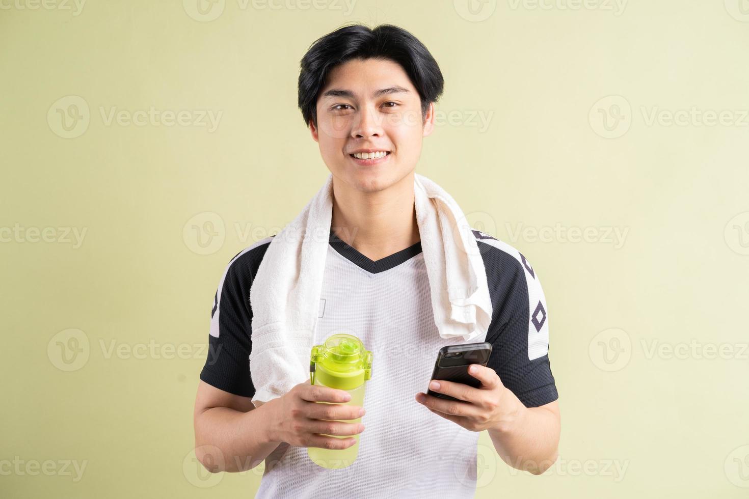 Hombre asiático sosteniendo agua y smartphone en mano sobre fondo verde foto