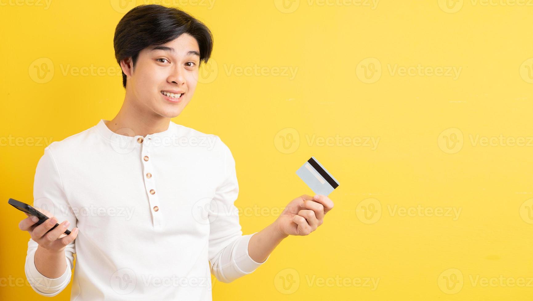 Hombre asiático sosteniendo una tarjeta bancaria en la mano sobre un fondo amarillo foto