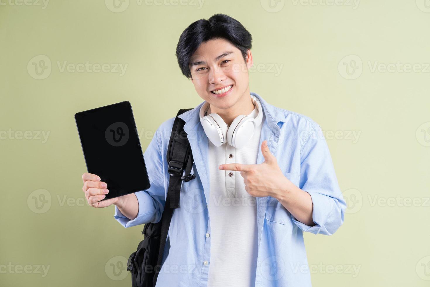 Estudiante asiático masculino está apuntando con el dedo a la tableta con una pantalla en blanco foto