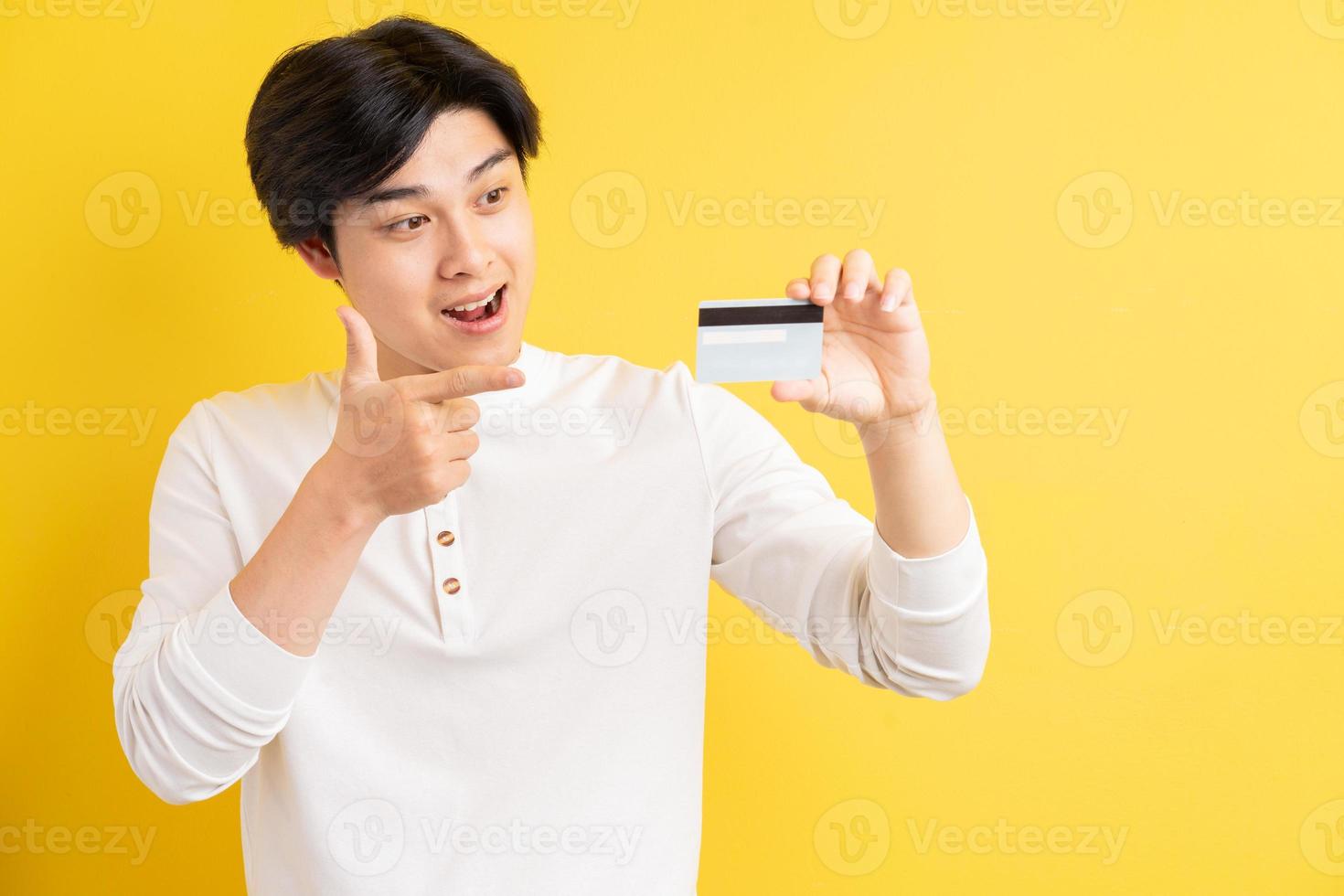 Hombre asiático sosteniendo una tarjeta bancaria en la mano sobre un fondo amarillo foto