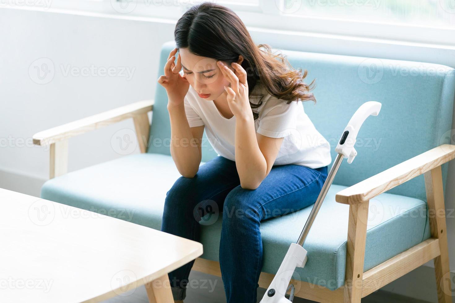 Mujer asiática sentada en una silla con una expresión cansada mientras limpia la casa foto