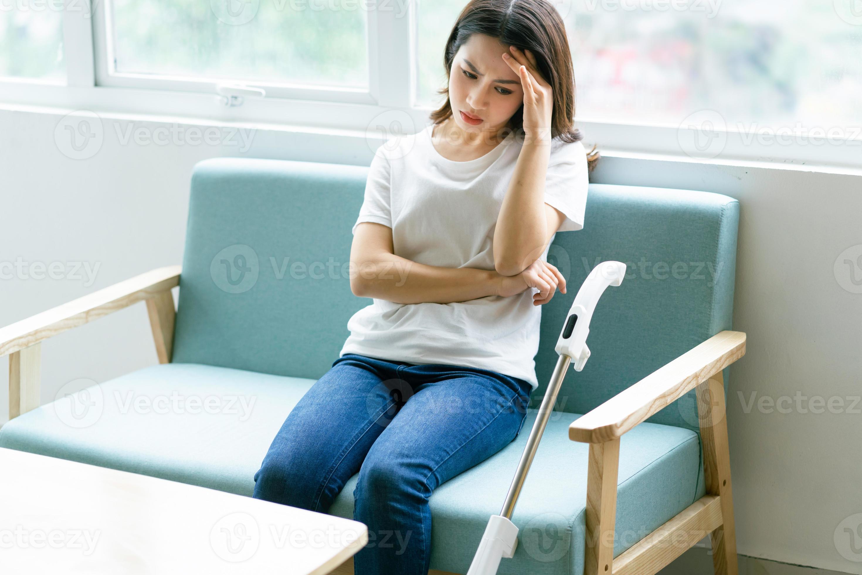 Mujer asiática sentada en una silla con una expresión cansada mientras limpia la casa foto