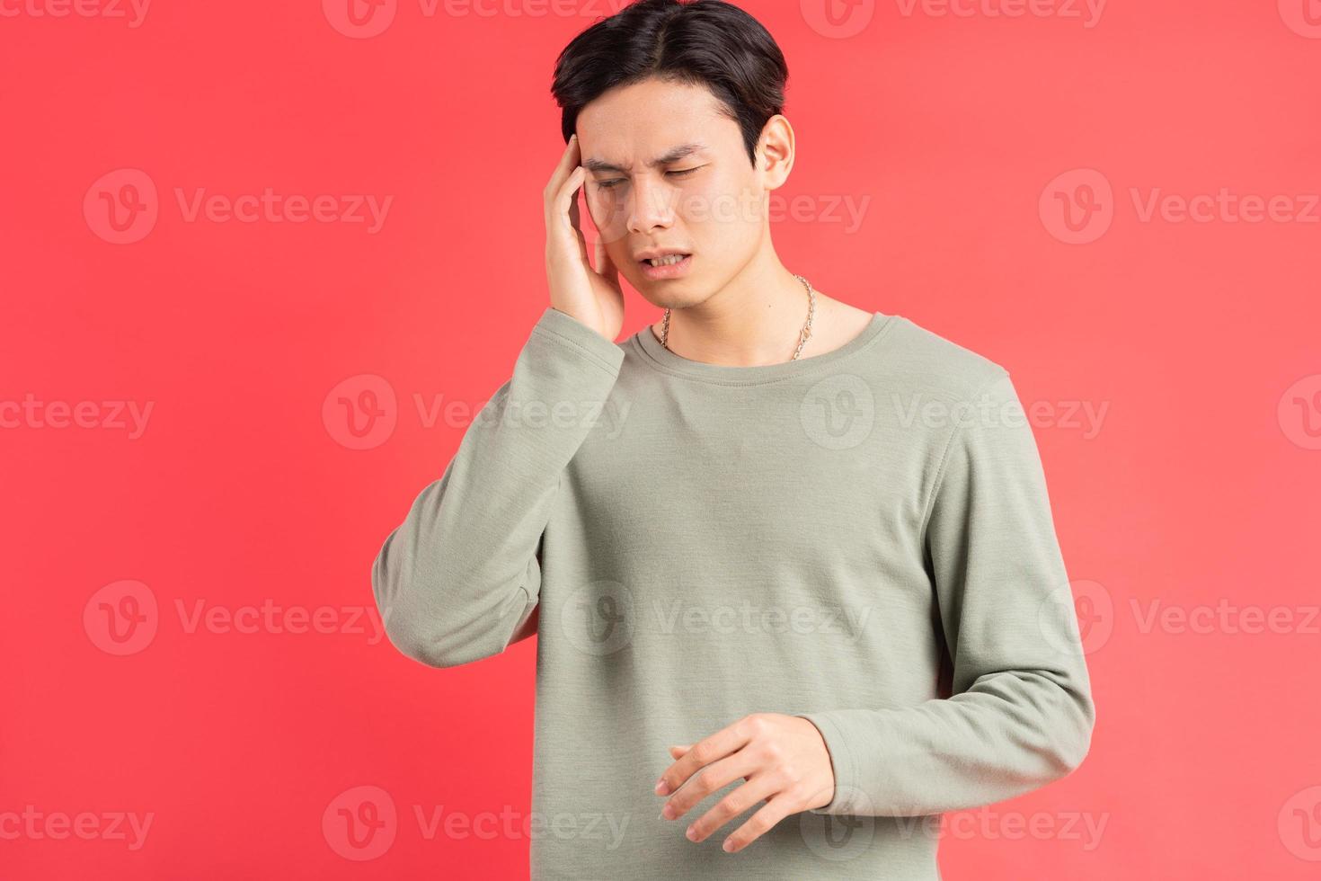 Una foto de un apuesto hombre asiático frotándose la cabeza con la mano debido a su migraña