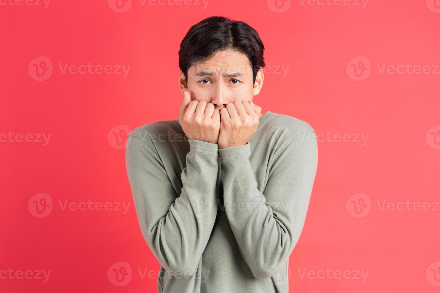 A photo of a handsome Asian man covering his face with his hands in fear