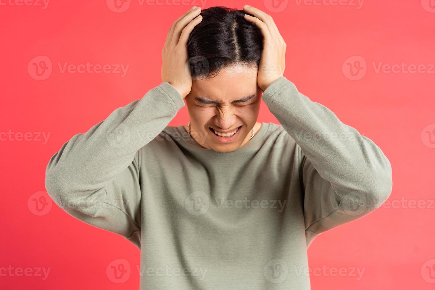 A photo of a handsome Asian man holding his head with both hands in fatigue