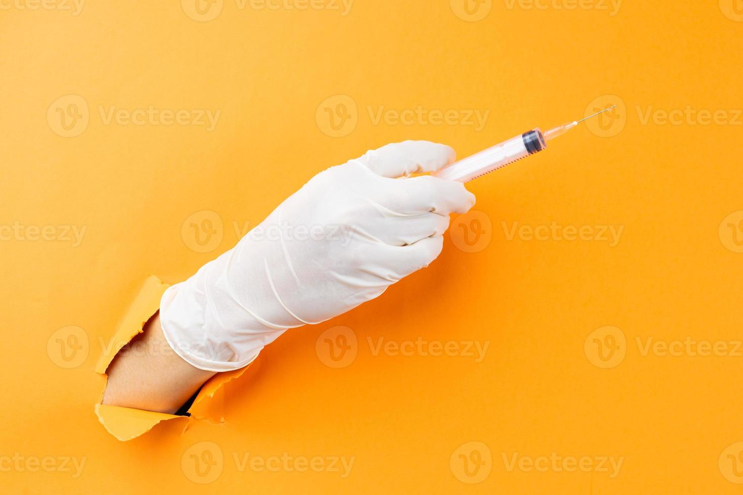 Hand holding syringe protruding from background photo