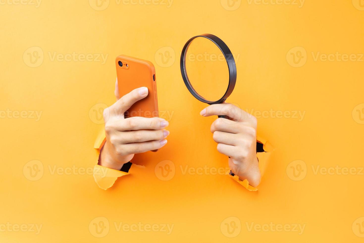 Hand holding magnifying glass and phone protruding from background photo