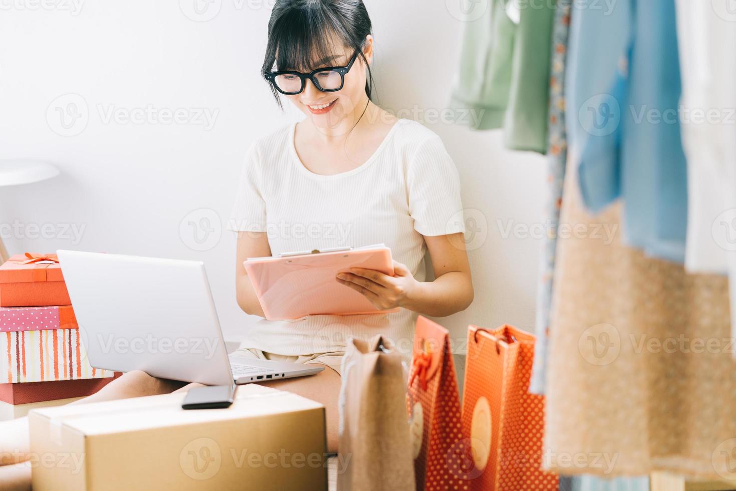 Young Asian businesswoman is sitting on the floor to check her orders from e-commerce sites photo