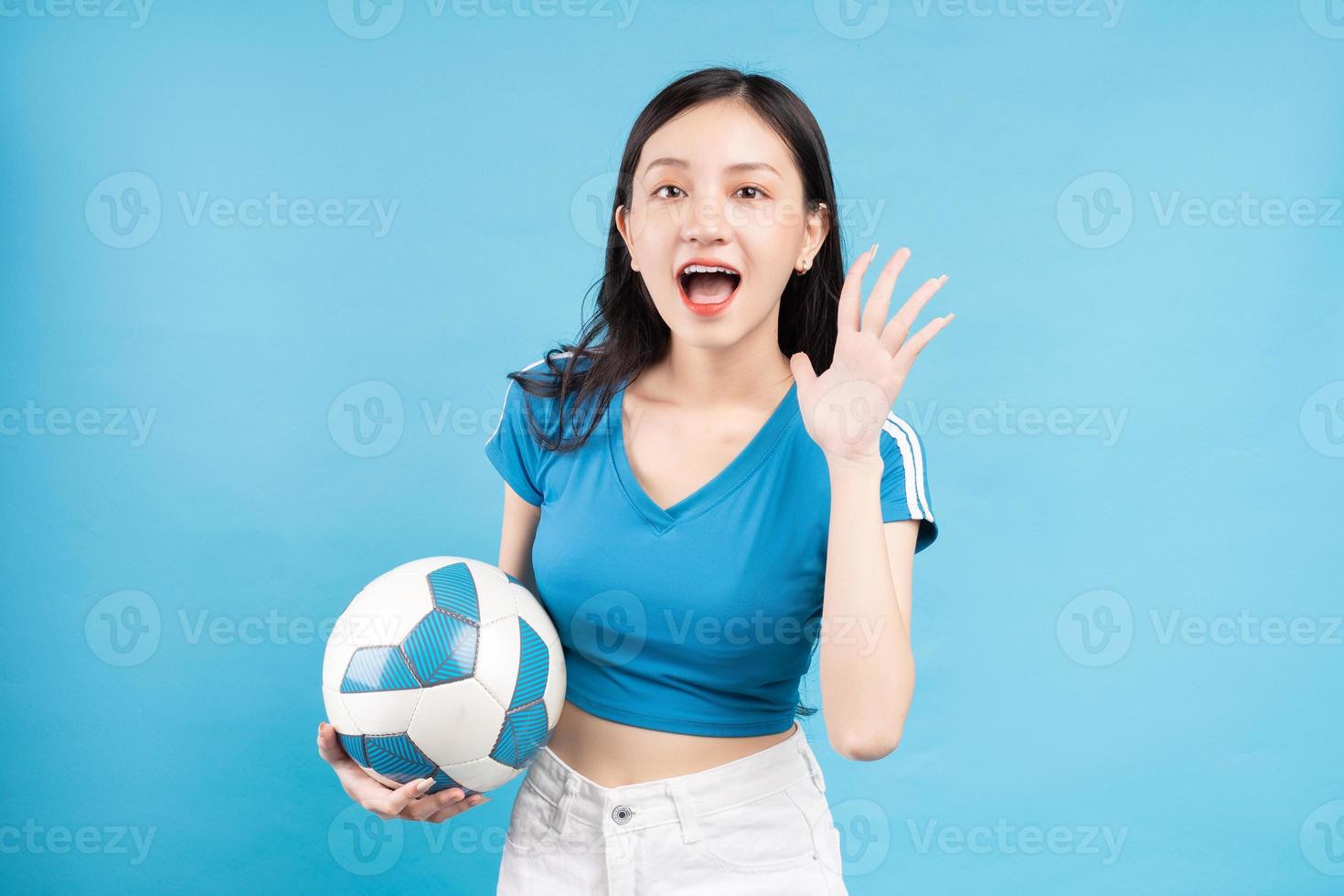 Hermosa mujer asiática posando con balón de fútbol sobre fondo azul. foto