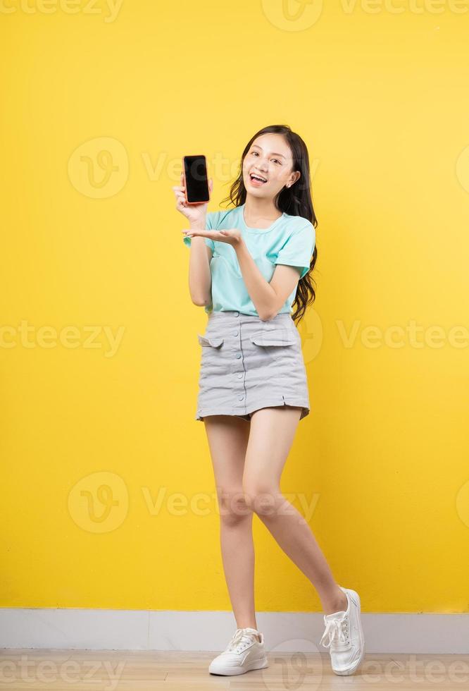 Young Asian girl holding smartphone on yellow background photo