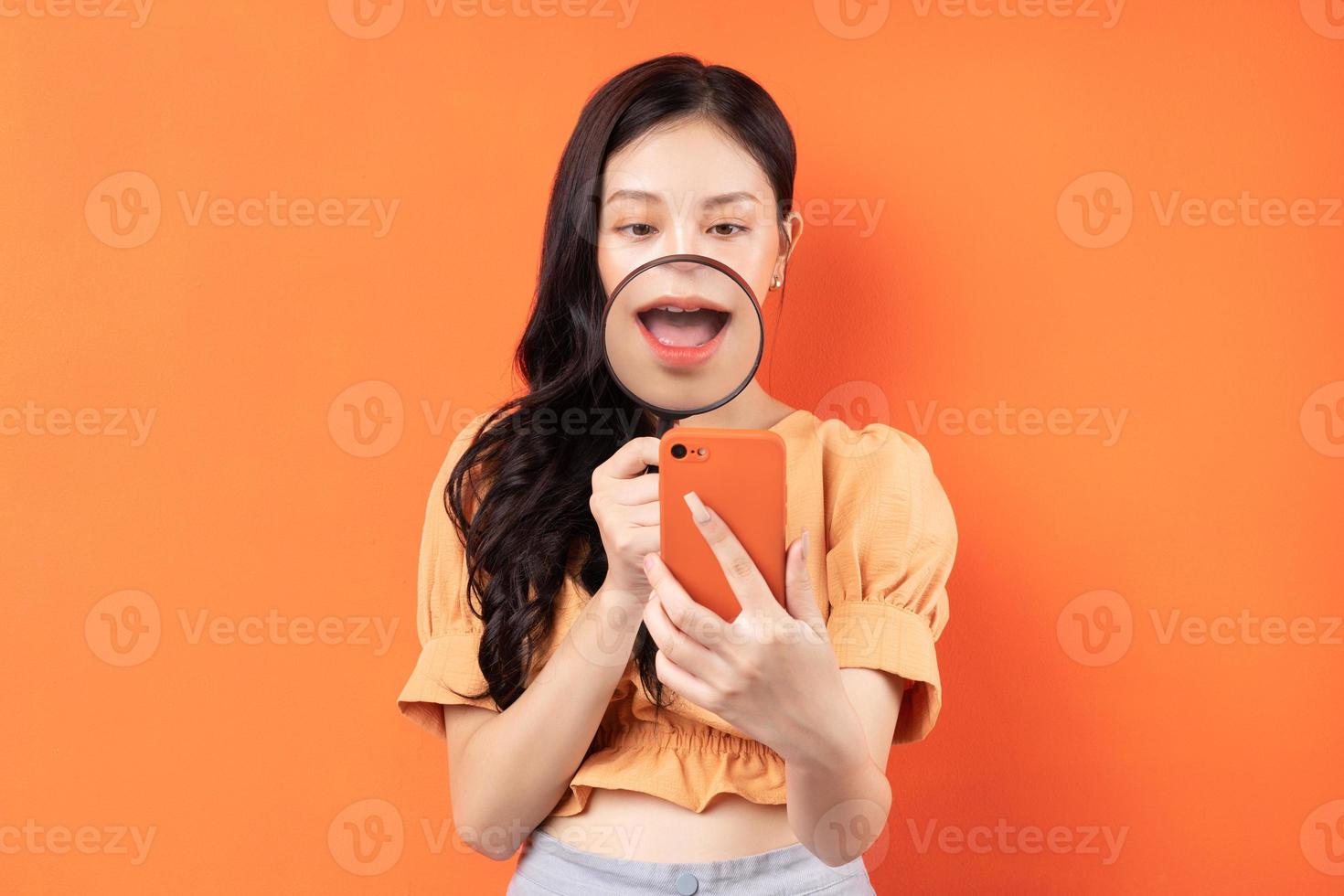 Woman holding a magnifying glass looking at her phone with a surprised expression photo