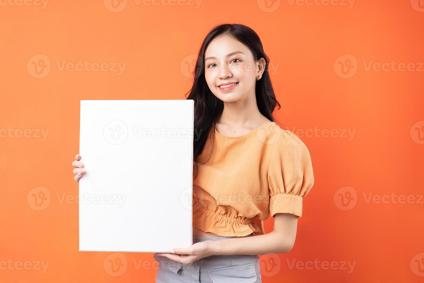Joven mujer asiática sosteniendo una pizarra blanca sobre fondo naranja foto