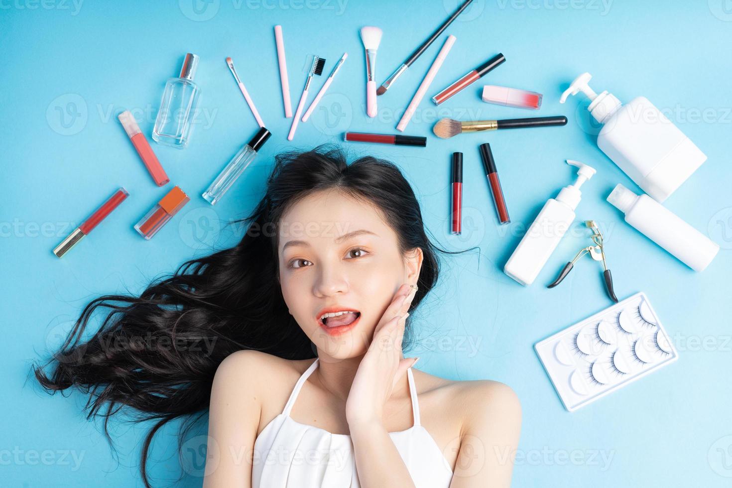 Asian woman lying on blue background with makeup around photo