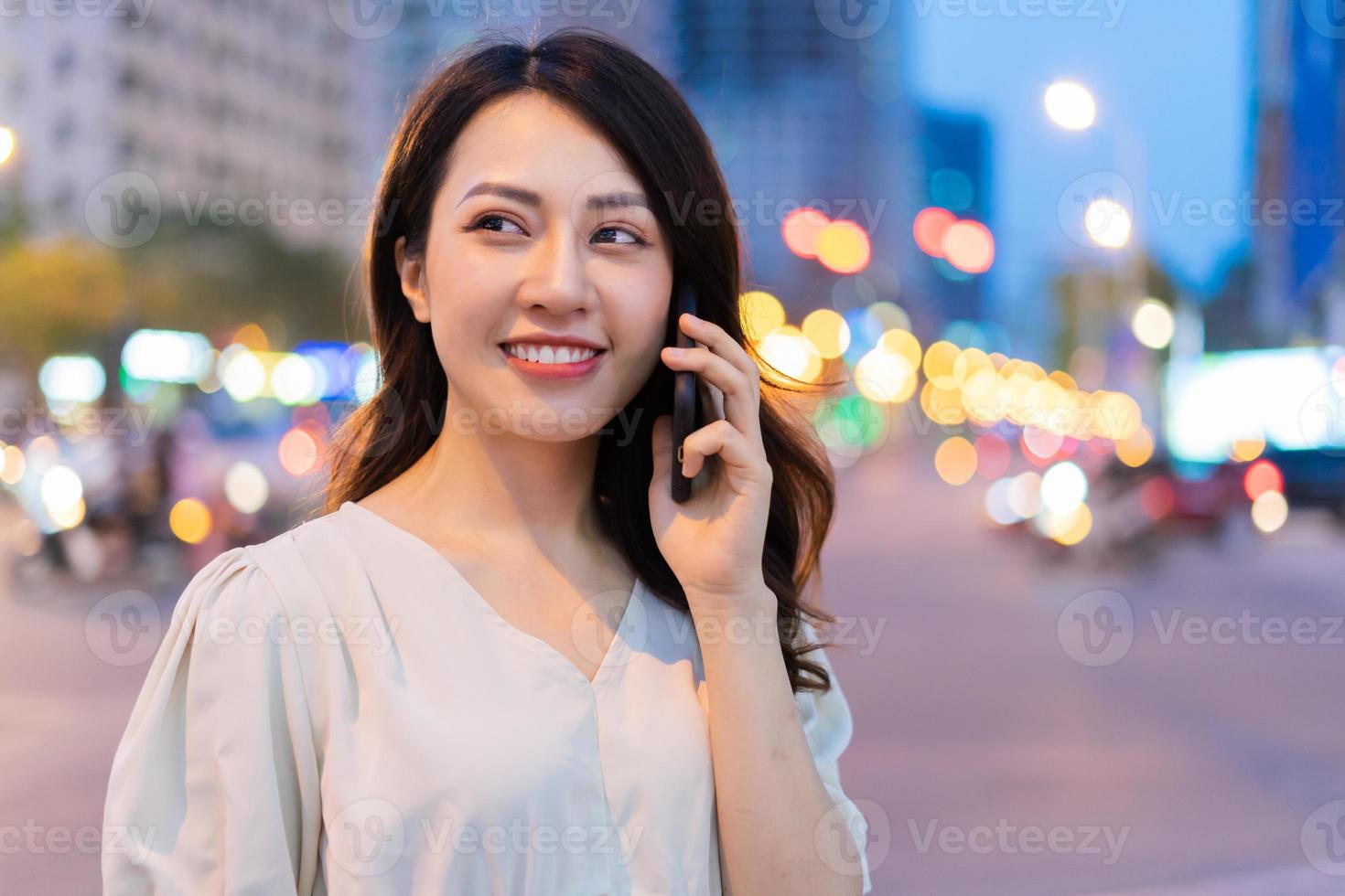 Joven mujer asiática llamando mientras camina por la calle por la noche foto