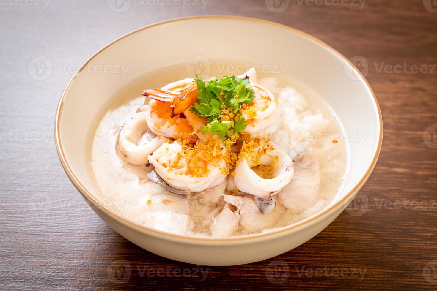 Porridge or boiled rice soup with seafood of shrimp, squid, and fish in a bowl photo