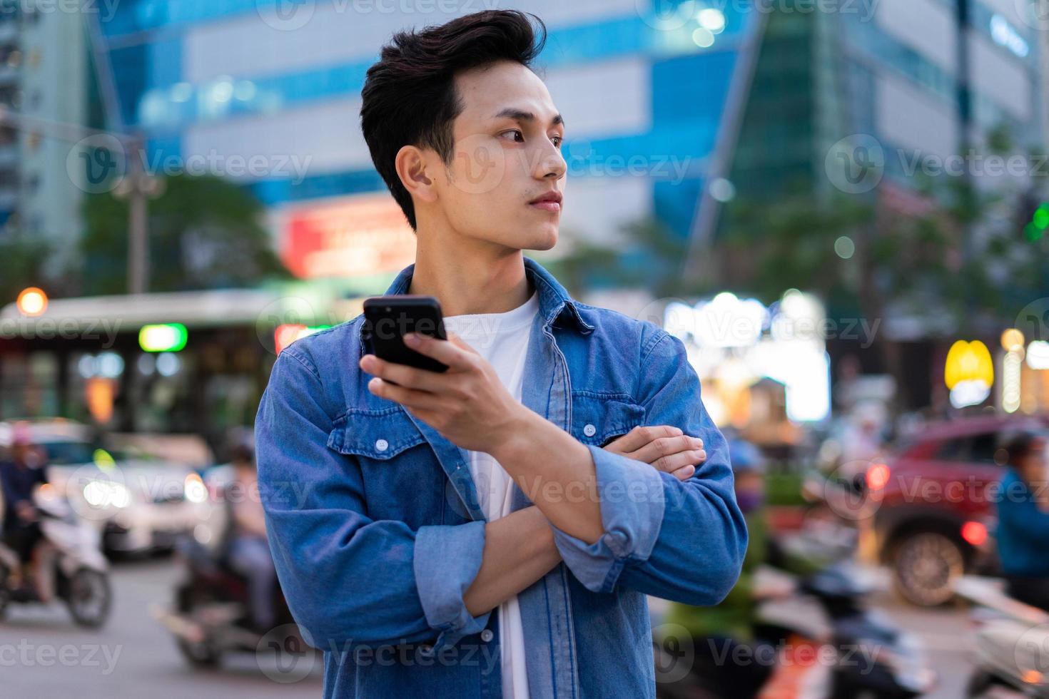 Young Asian man using smartphone while walking on the street at night photo