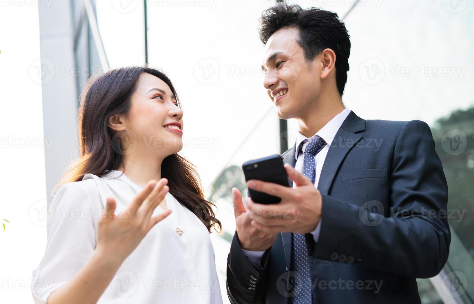 Dos hombres de negocios asiáticos que usan teléfonos inteligentes y hablan juntos foto
