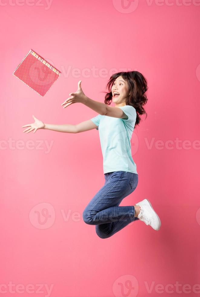 Mujer sosteniendo caja de regalo saltando con expresión alegre en el fondo foto