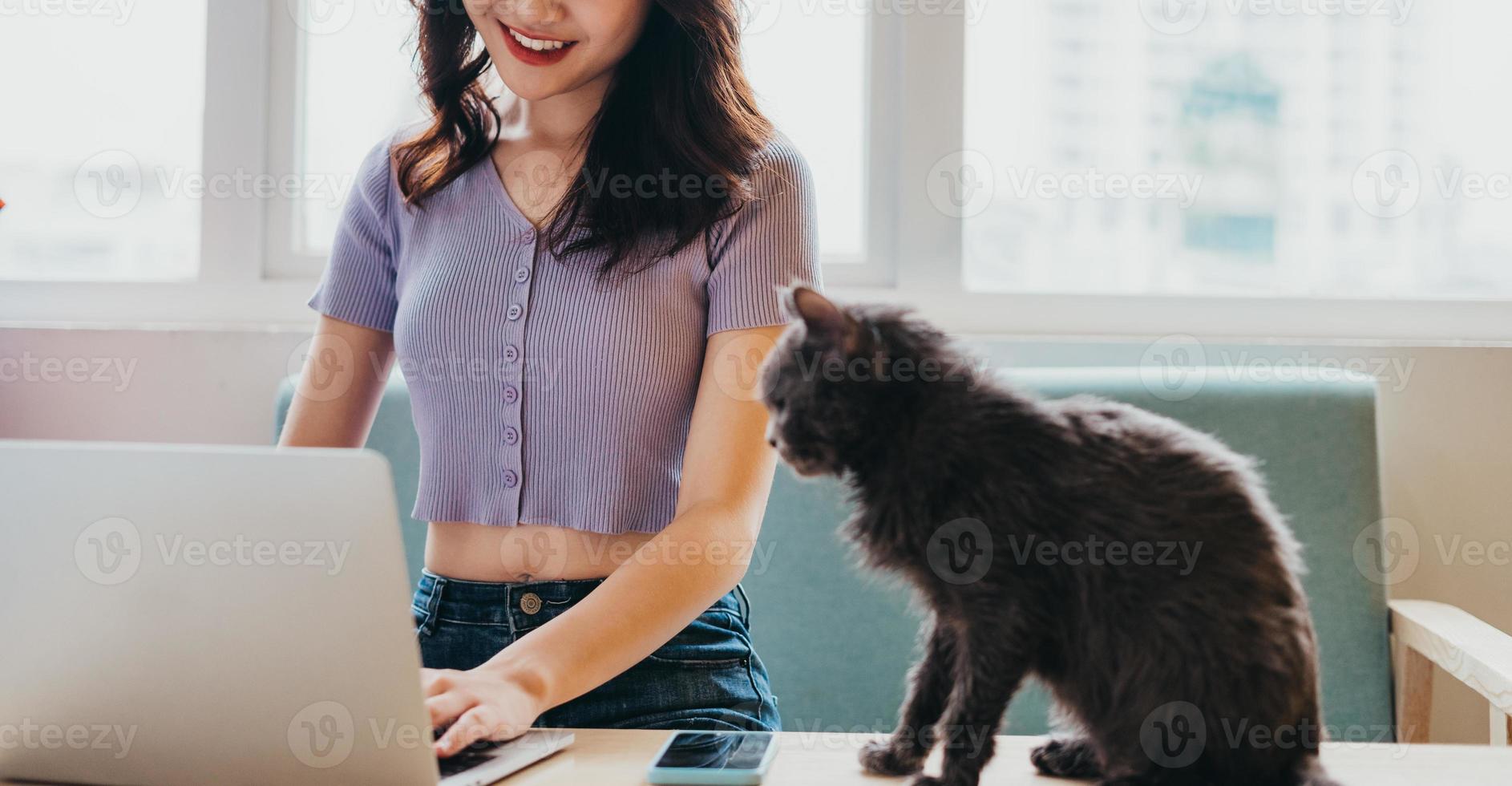 Young girl sitting working on sofa and cat sitting next to laptop photo