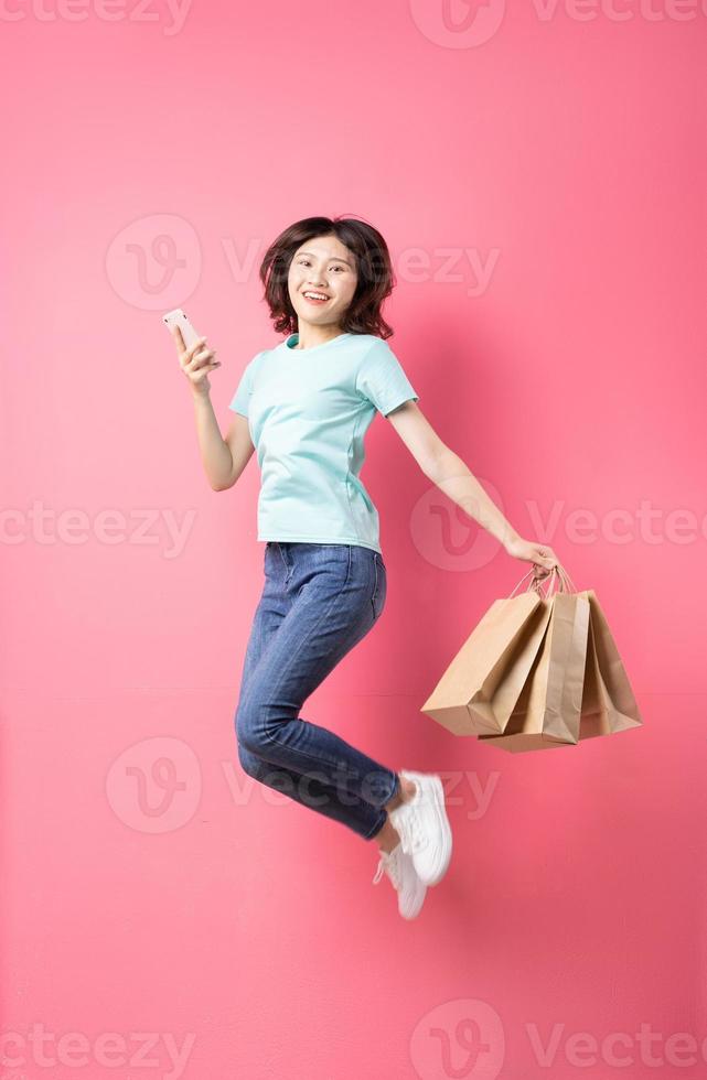 Mujer sosteniendo teléfono y bolsa de compras saltando con expresión alegre en el fondo foto