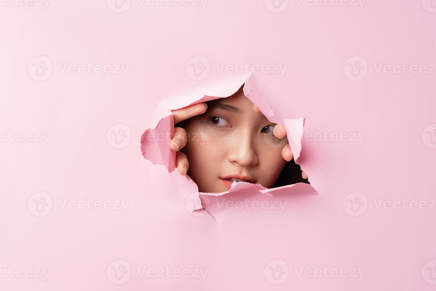 Young Asian woman poked her head through the torn paper photo