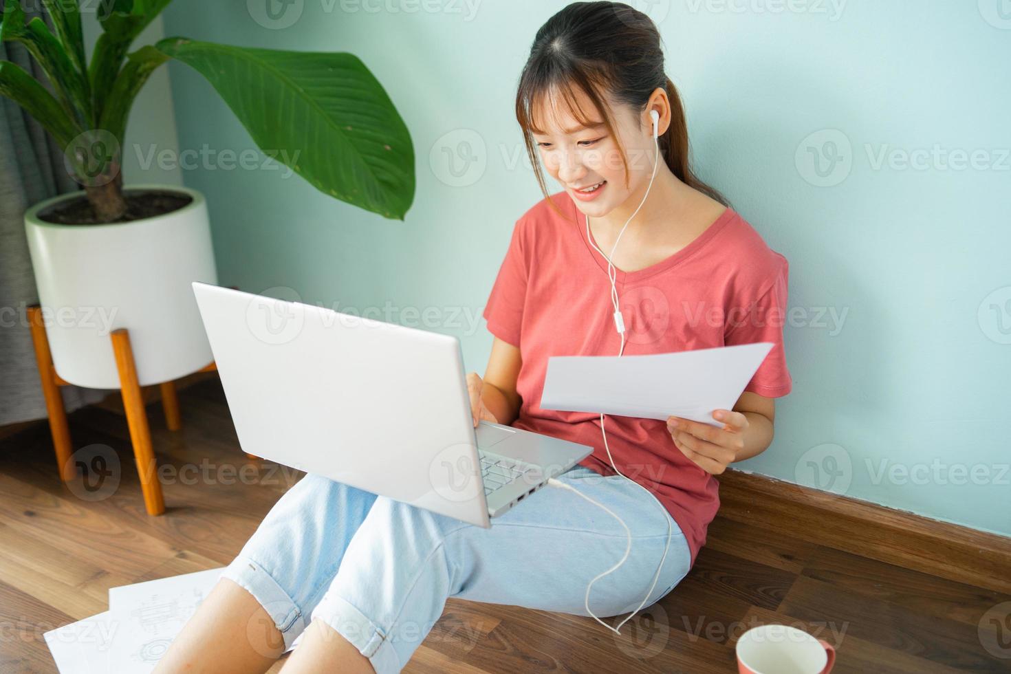 Mujer asiática sentada en el suelo mientras trabaja desde casa foto