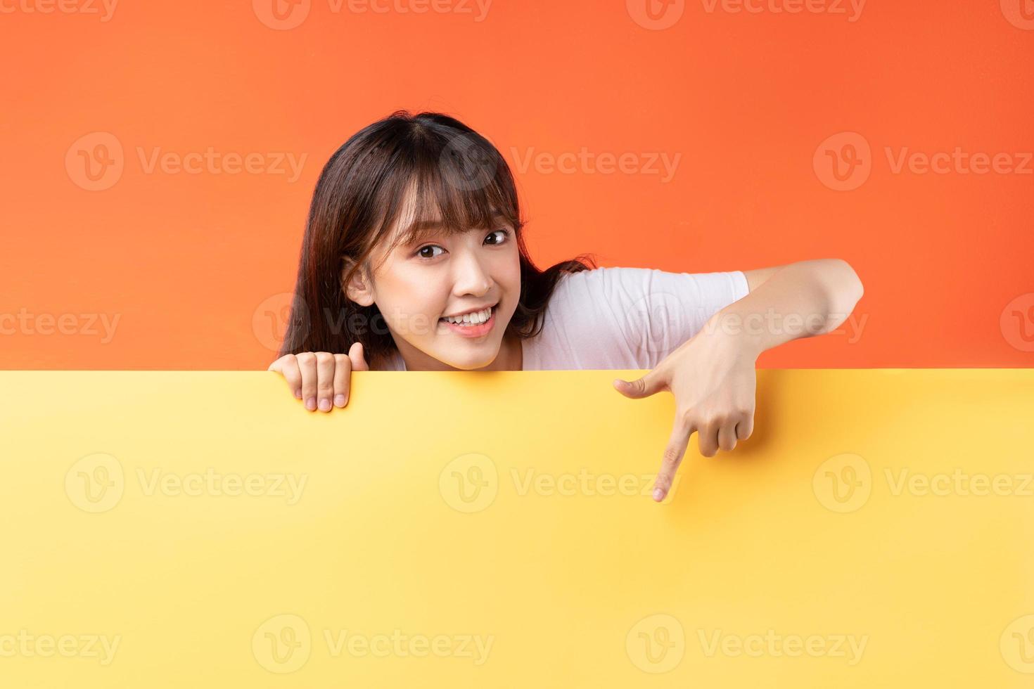 Young Asian girl pointing her finger down on yellow and orange background photo