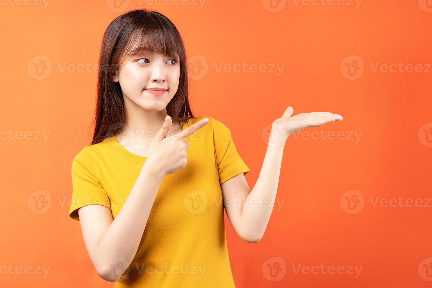 Imagen de una joven asiática con camiseta amarilla sobre fondo naranja foto