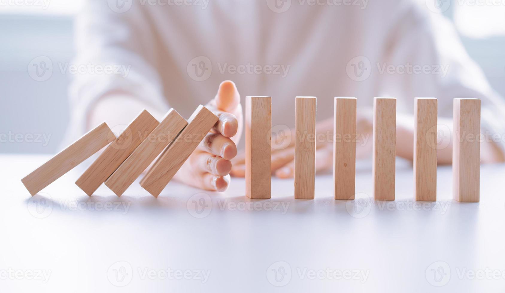 La mano de la mujer detiene el efecto de crisis empresarial de dominó de madera, concepto de protección de riesgos foto