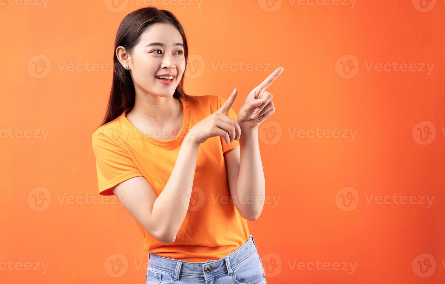 Imagen de la joven mujer asiática con camiseta naranja sobre fondo naranja foto