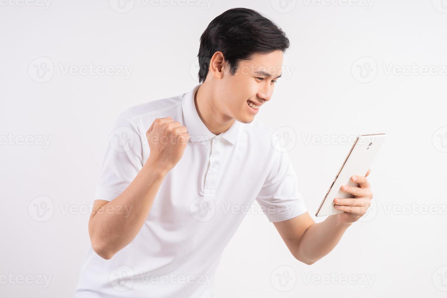 Image of happy young man standing on isolated white wall background. Look aside using the tablet as a winner gesture. photo