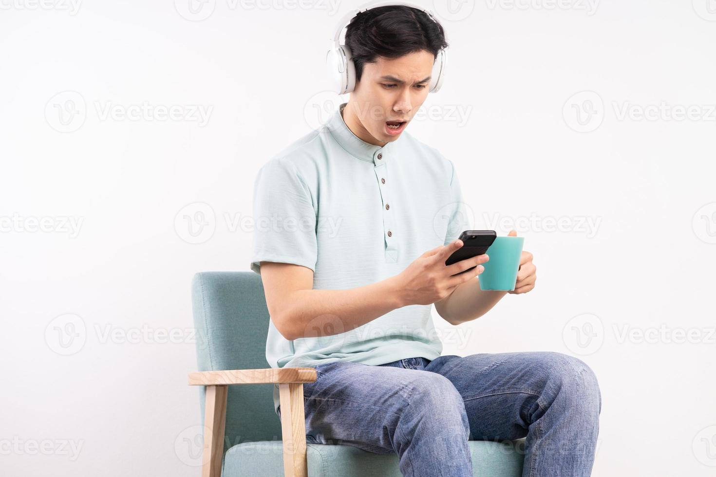 joven sentado en el sofá escuchando música. mirando el teléfono con una expresión de sorpresa foto