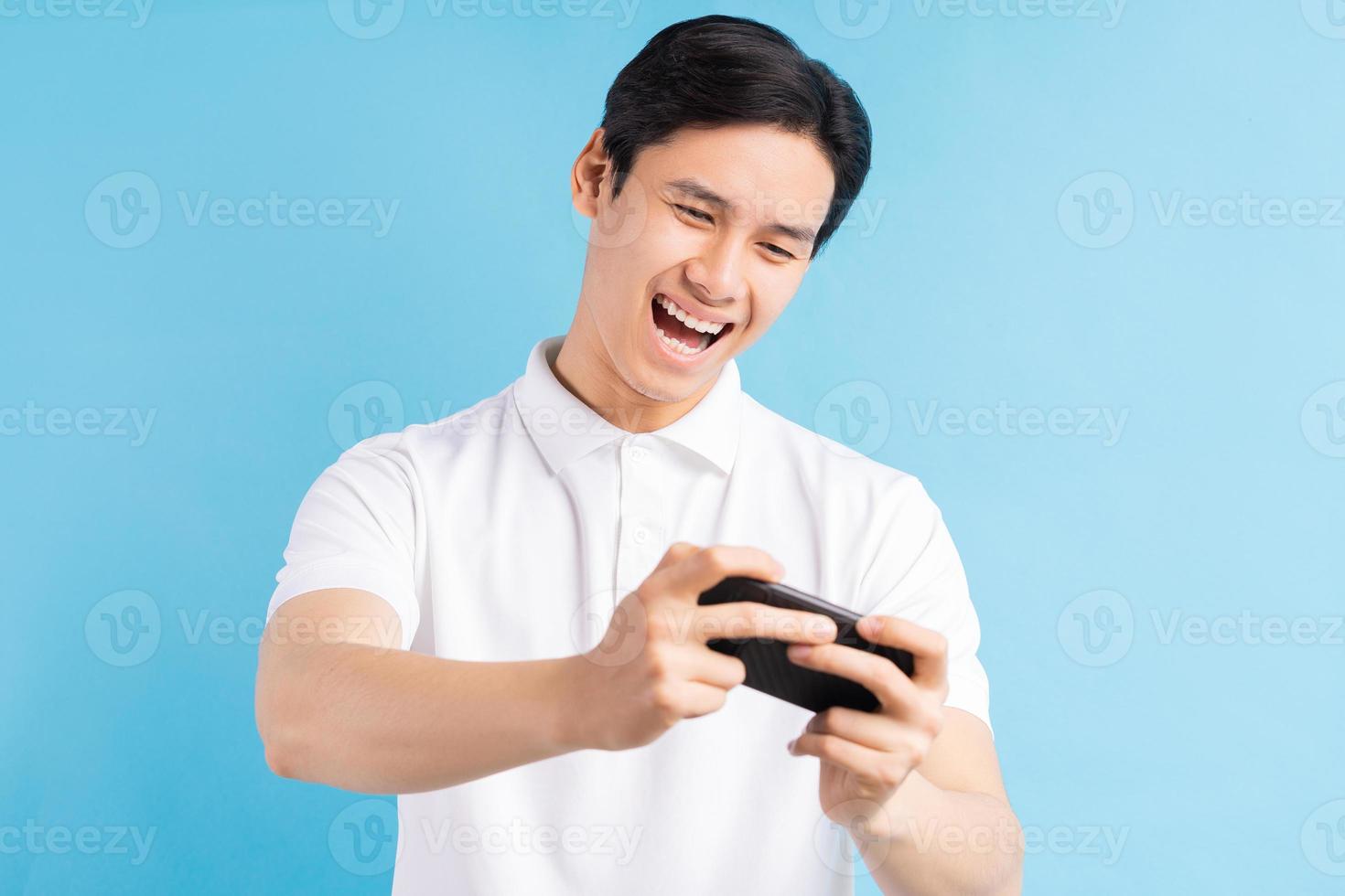 Excited handsome young male gamer playing online game on smartphone isolated on blue background photo