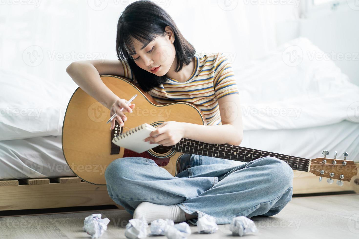 Joven asiática está practicando guitarra en casa y componiendo música foto